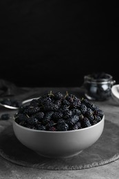 Bowl of delicious ripe black mulberries on grey table