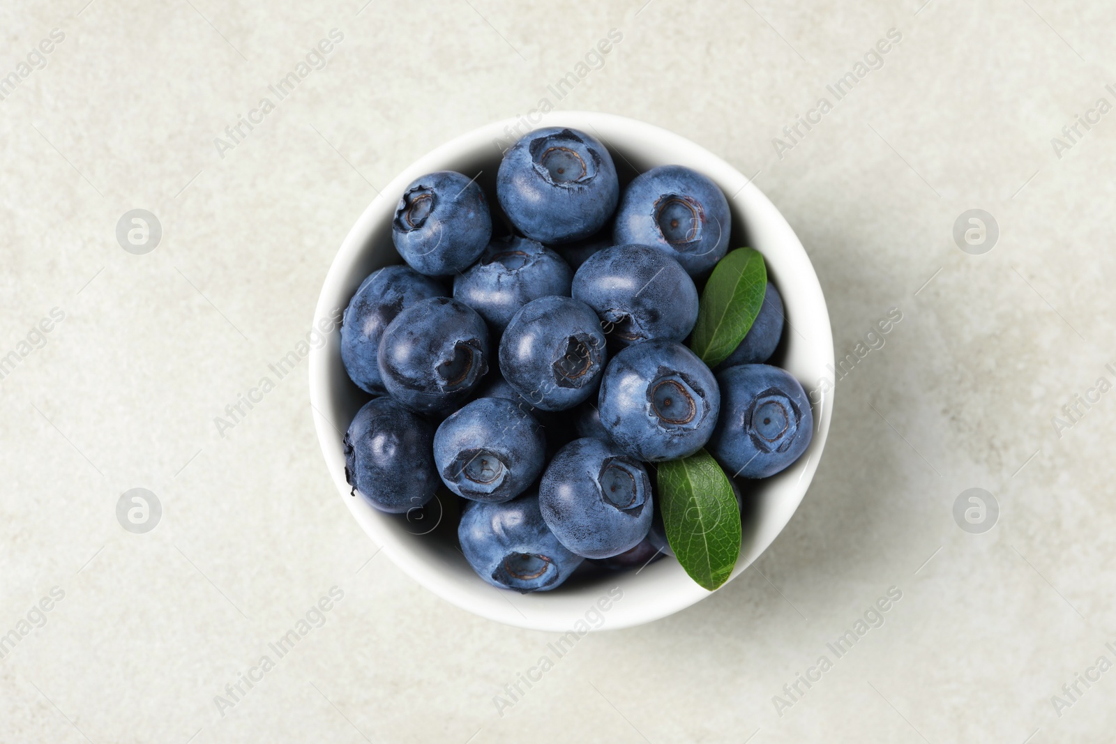 Photo of Bowl of fresh tasty blueberries on light grey table, top view