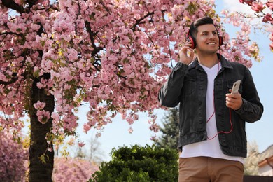 Happy man with smartphone listening to audiobook outdoors on spring day