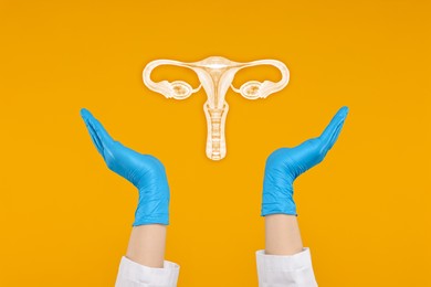 Doctor and illustration of female reproductive system on orange background, closeup