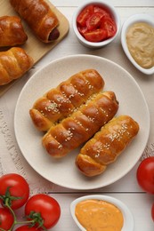 Delicious sausage rolls and ingredients on white wooden table, flat lay