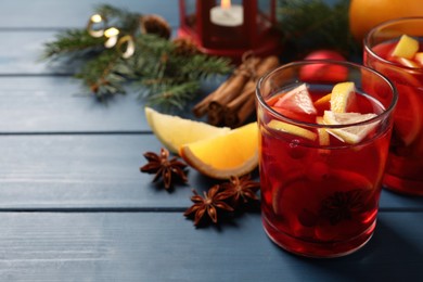 Photo of Delicious punch drink with cranberries and orange on blue wooden table. Space for text