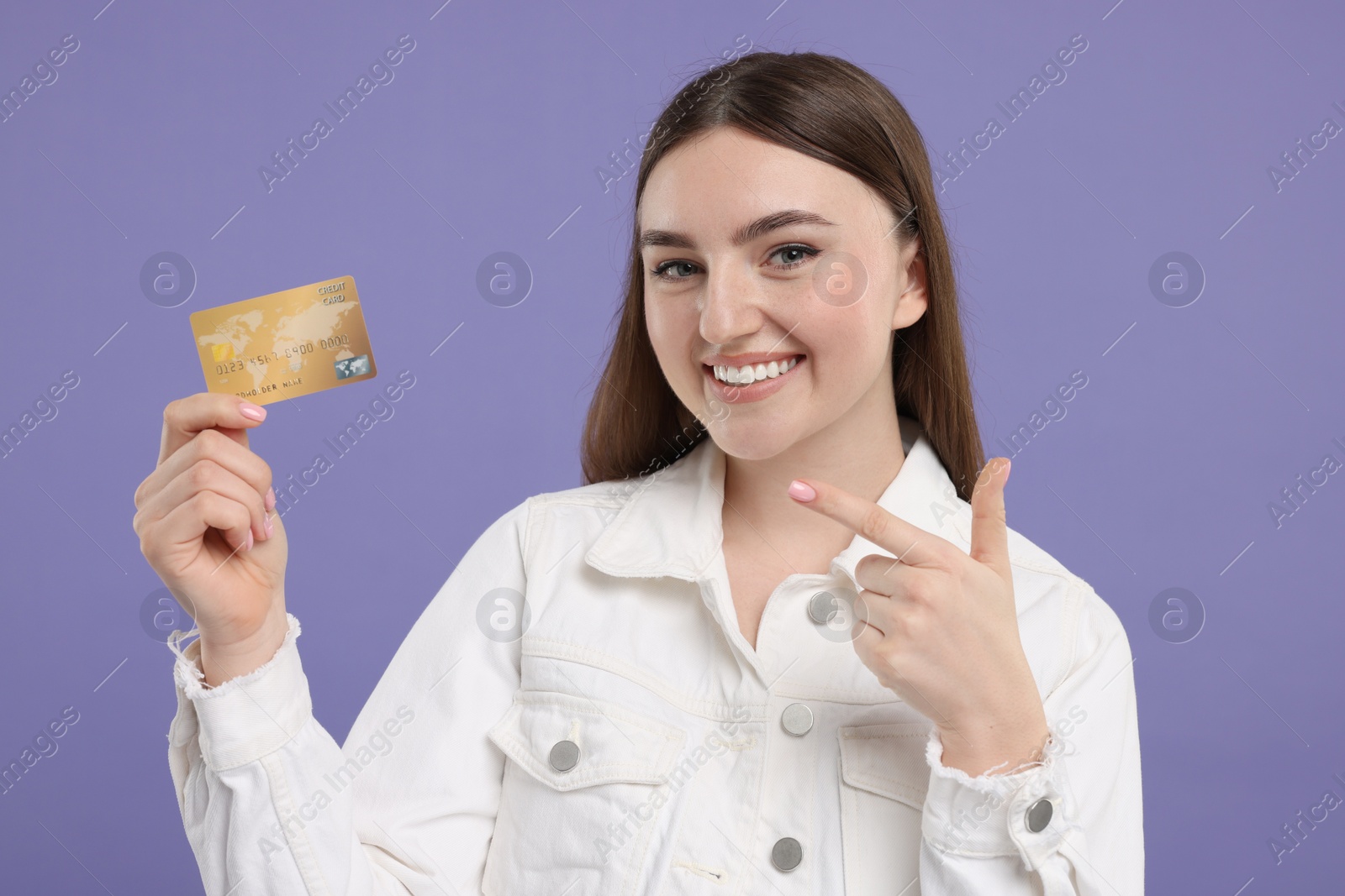 Photo of Happy woman pointing at credit card on purple background