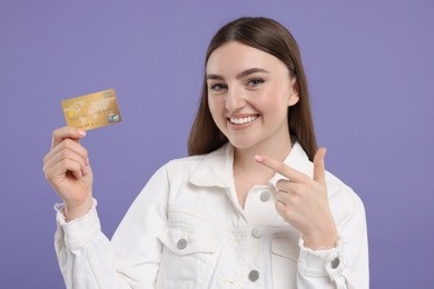 Photo of Happy woman pointing at credit card on purple background