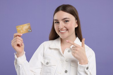 Happy woman pointing at credit card on purple background