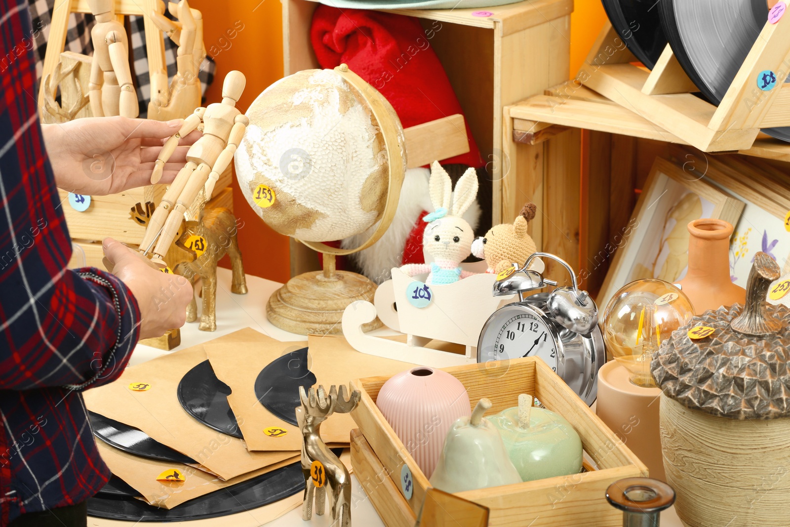 Photo of Woman holding wooden figure near table with different stuff indoors, closeup. Garage sale