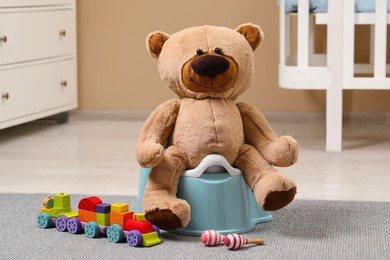 Photo of Teddy bear on light blue baby potty and toys in room. Toilet training
