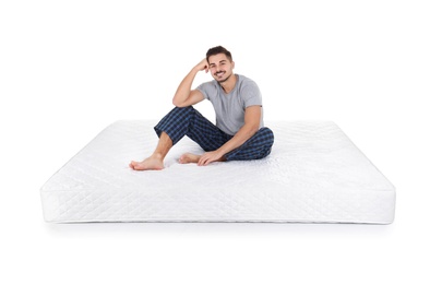 Young man sitting on mattress against white background