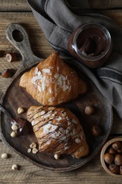 Delicious croissants with chocolate and nuts on wooden table, flat lay