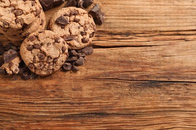 Many delicious chocolate chip cookies on wooden table, top view. Space for text