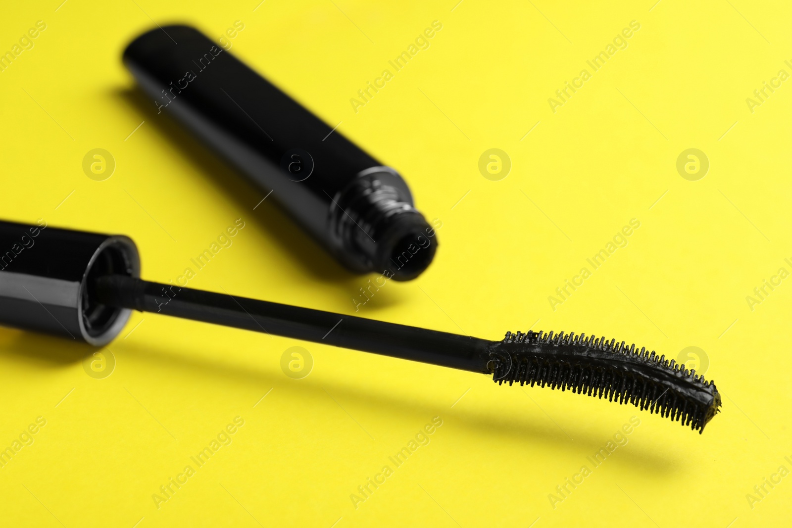Photo of Mascara for eyelashes on yellow background, closeup. Makeup product