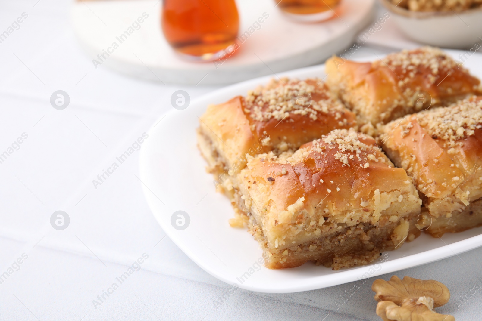 Photo of Eastern sweets. Pieces of tasty baklava and tea on white tiled table, closeup. Space for text