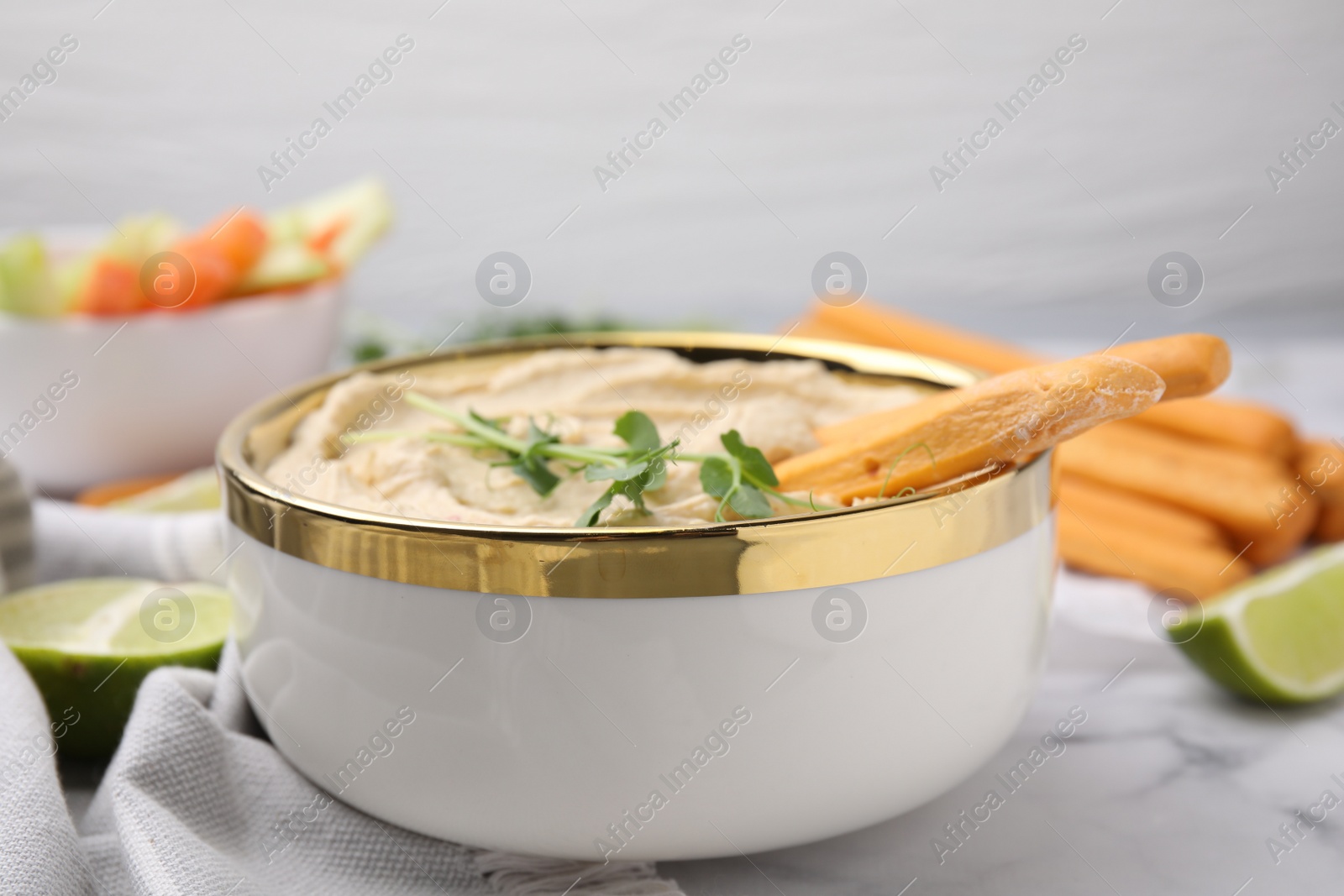 Photo of Delicious hummus with grissini sticks served on white marble table, closeup