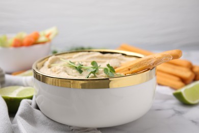 Delicious hummus with grissini sticks served on white marble table, closeup