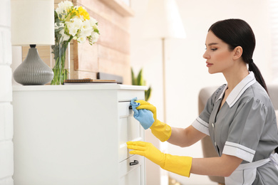 Young chambermaid wiping dust from furniture in hotel room