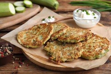Photo of Delicious zucchini fritters with sour cream served on wooden table, closeup