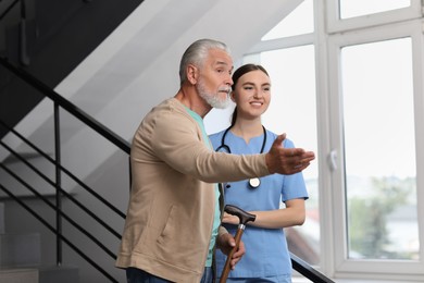 Photo of Young healthcare worker assisting senior man on stairs indoors