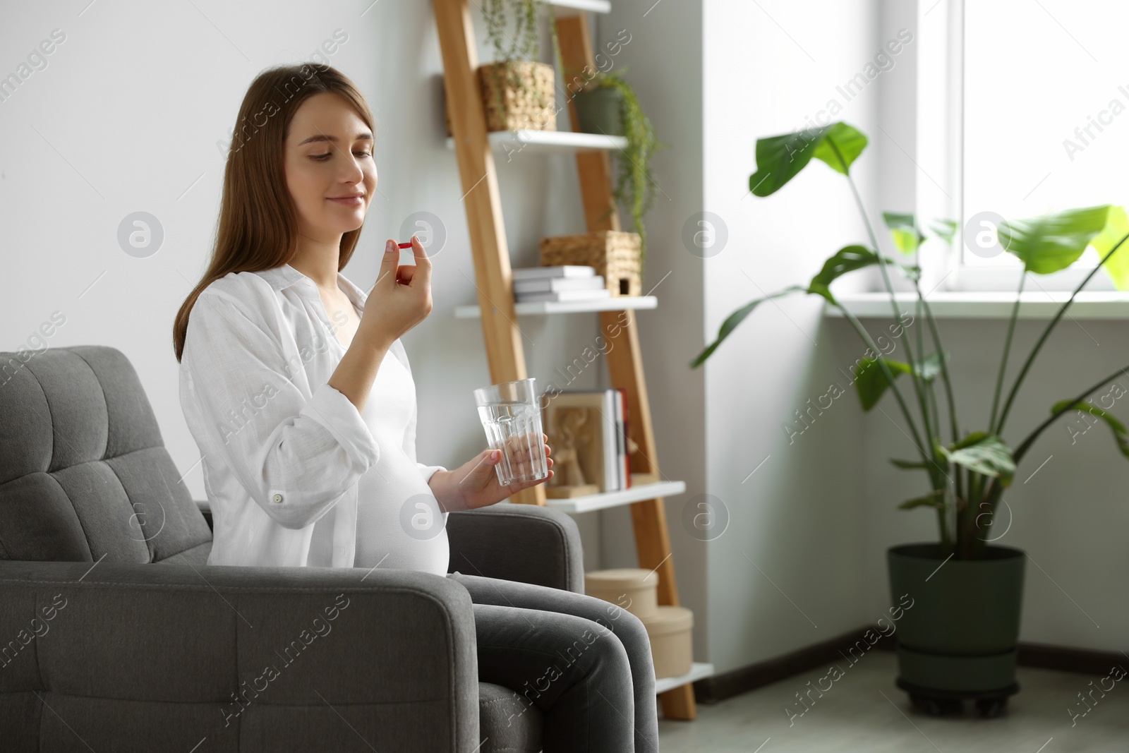 Photo of Beautiful pregnant woman holding pill and glass with water at home