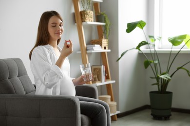 Beautiful pregnant woman holding pill and glass with water at home