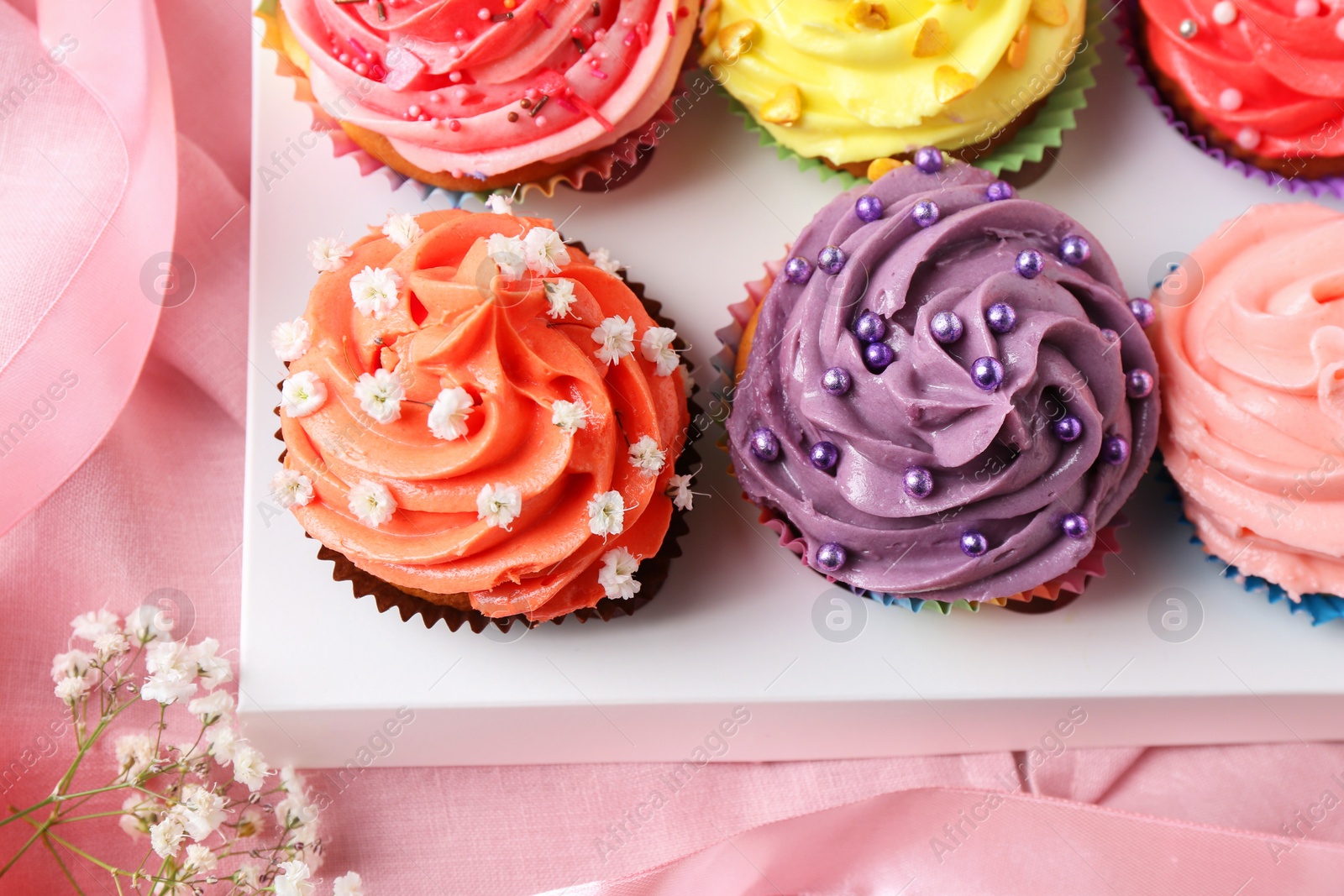 Photo of Delicious cupcake with bright cream on pink fabric, top view