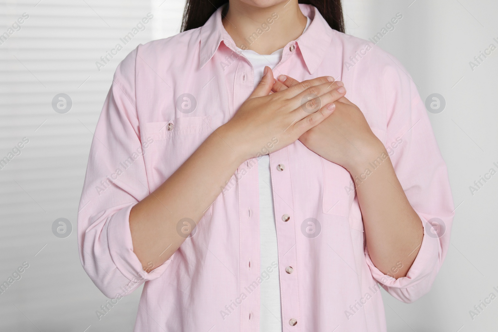 Photo of Thank you gesture. Grateful woman holding hands near heart indoors, closeup