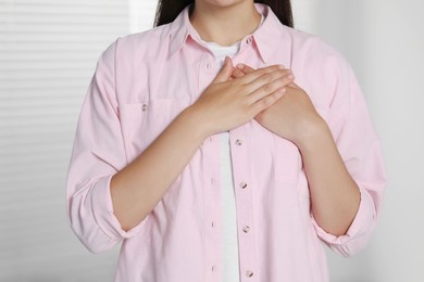 Photo of Thank you gesture. Grateful woman holding hands near heart indoors, closeup