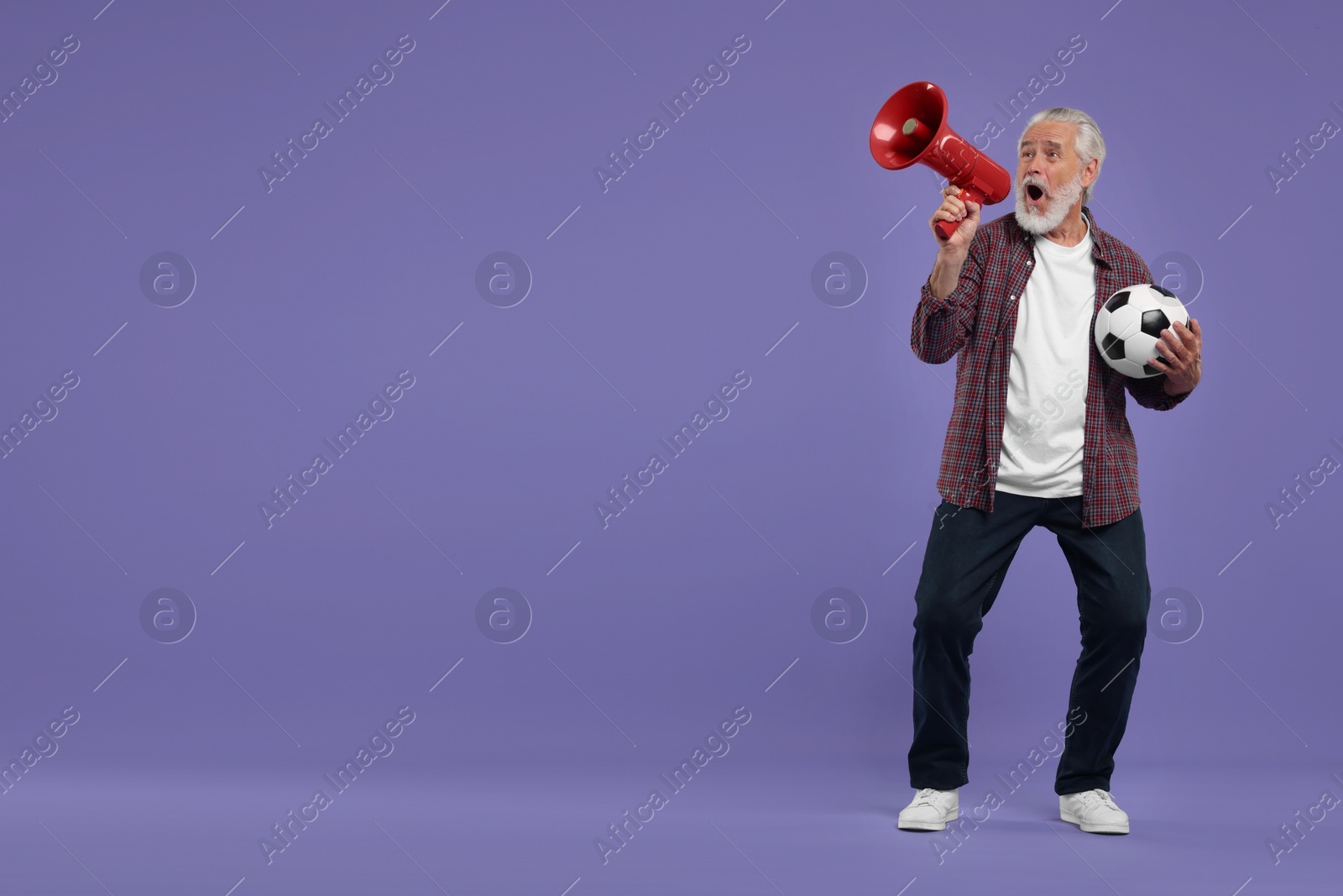 Photo of Emotional senior sports fan with soccer ball using megaphone on purple background, space for text