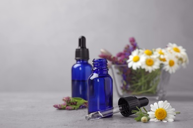 Photo of Bottles of essential oil and wildflowers on grey table, space for text