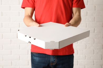 Young man with pizza box near white brick wall. Food delivery service