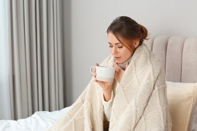 Photo of Sick woman with warm plaid and cup of drink in bed at home