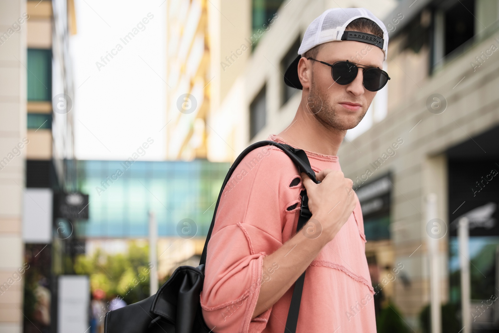 Photo of Handsome young man with stylish sunglasses and backpack on city street, space for text