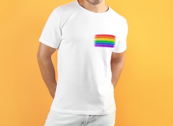 Image of Young man wearing white t-shirt with image of LGBT pride flag on orange background