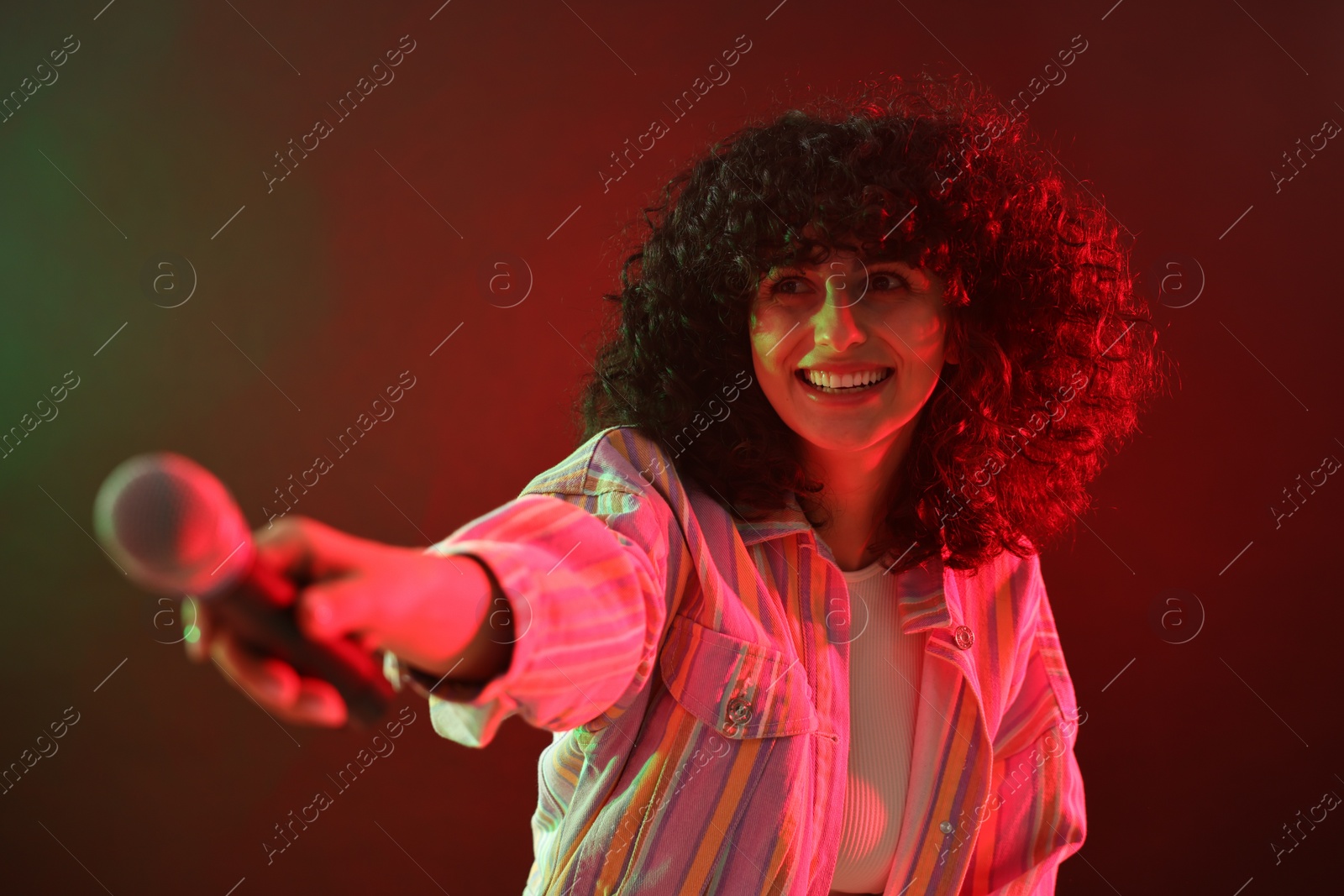 Photo of Beautiful young woman with microphone on color background in neon lights