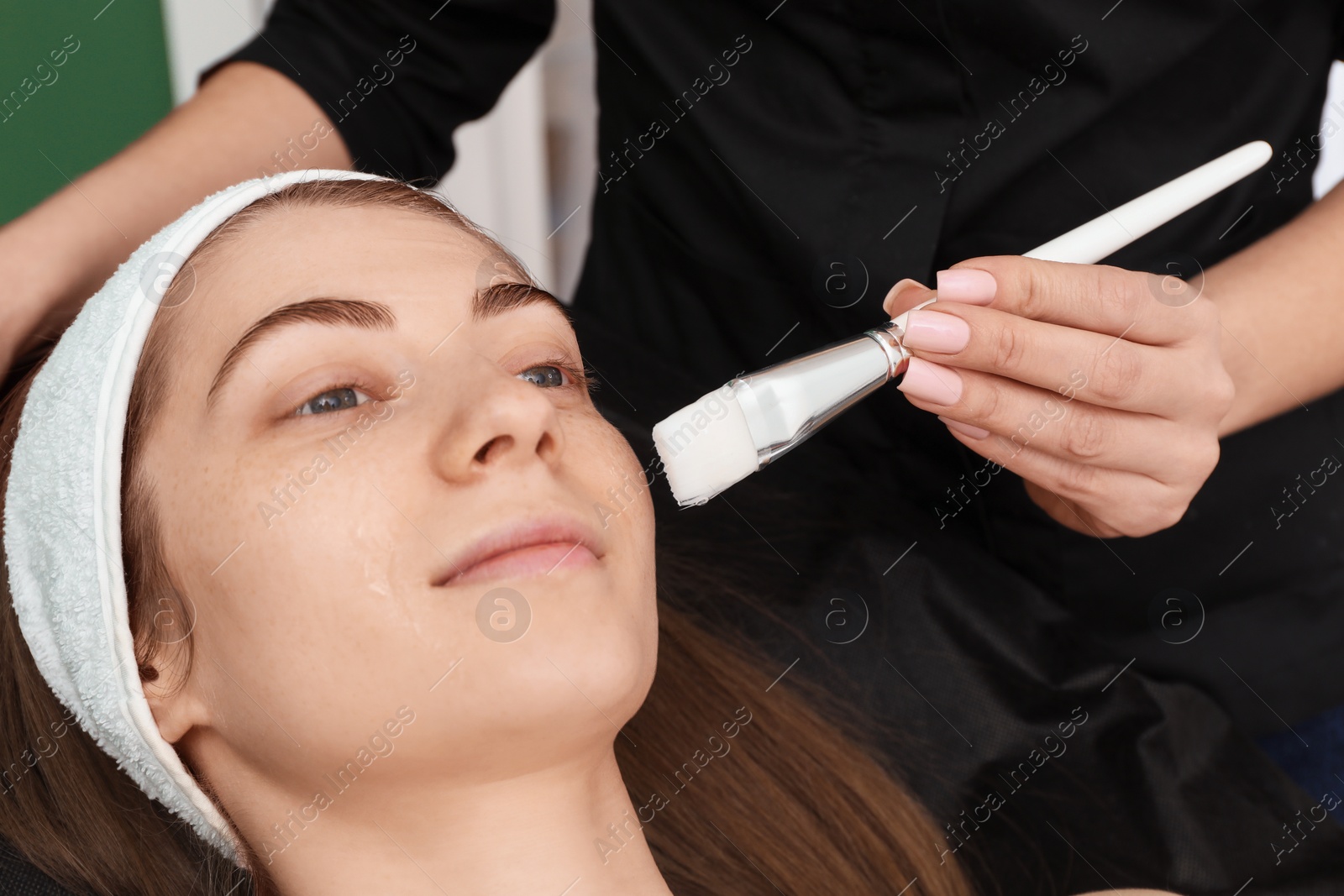 Photo of Cosmetologist applying mask on woman's face indoors, closeup