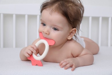Photo of Cute little baby with teether in comfortable crib at home