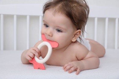 Cute little baby with teether in comfortable crib at home