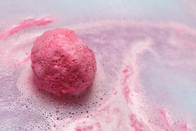 Pink bath bomb dissolving in water, closeup. Space for text