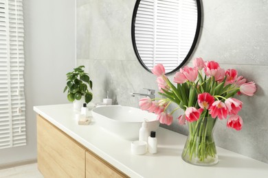 Vase with beautiful pink tulips and toiletries near sink in bathroom