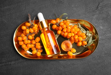 Photo of Ripe sea buckthorn and bottles of essential oil on black table, top view
