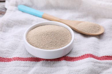 Photo of Bowl and spoon with active dry yeast on table, closeup