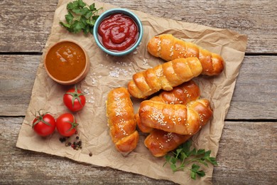 Delicious sausage rolls and ingredients on wooden table, top view