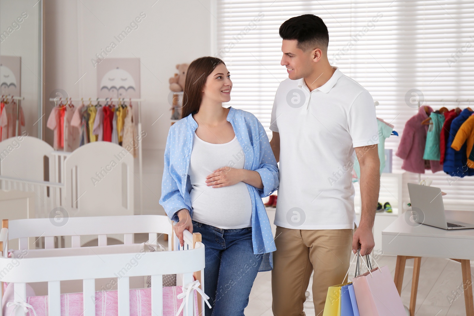 Photo of Happy pregnant woman and her husband with shopping bags choosing crib in store