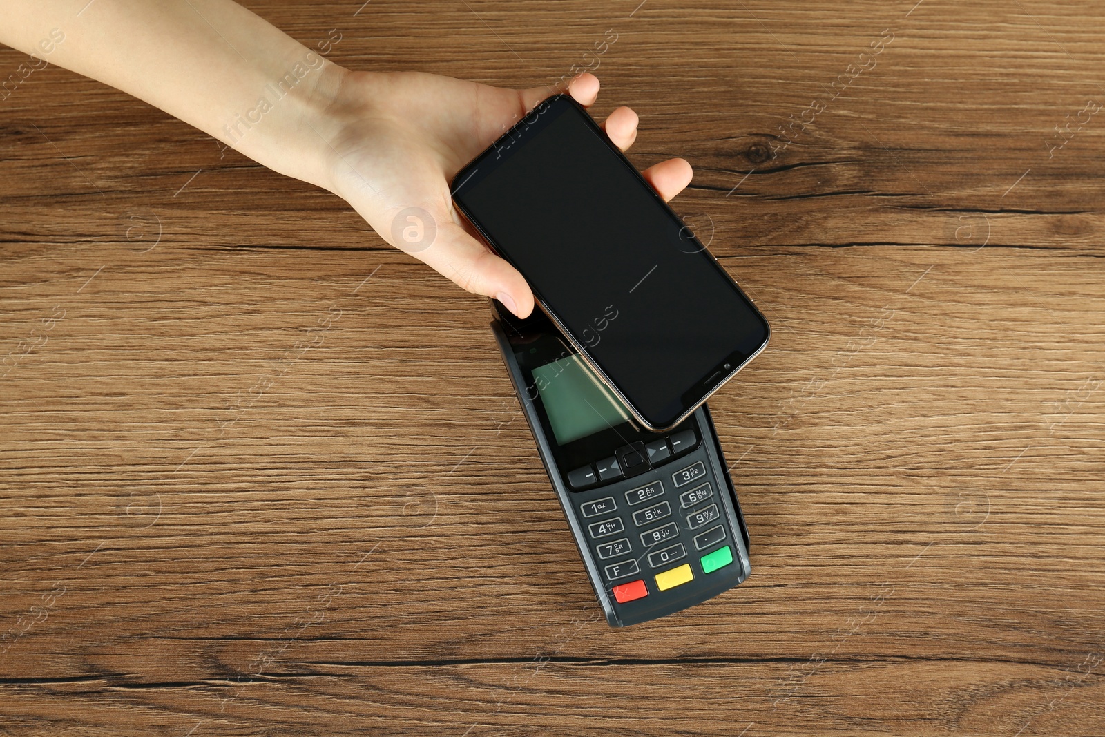 Photo of Woman with smartphone using modern payment terminal at wooden table, top view