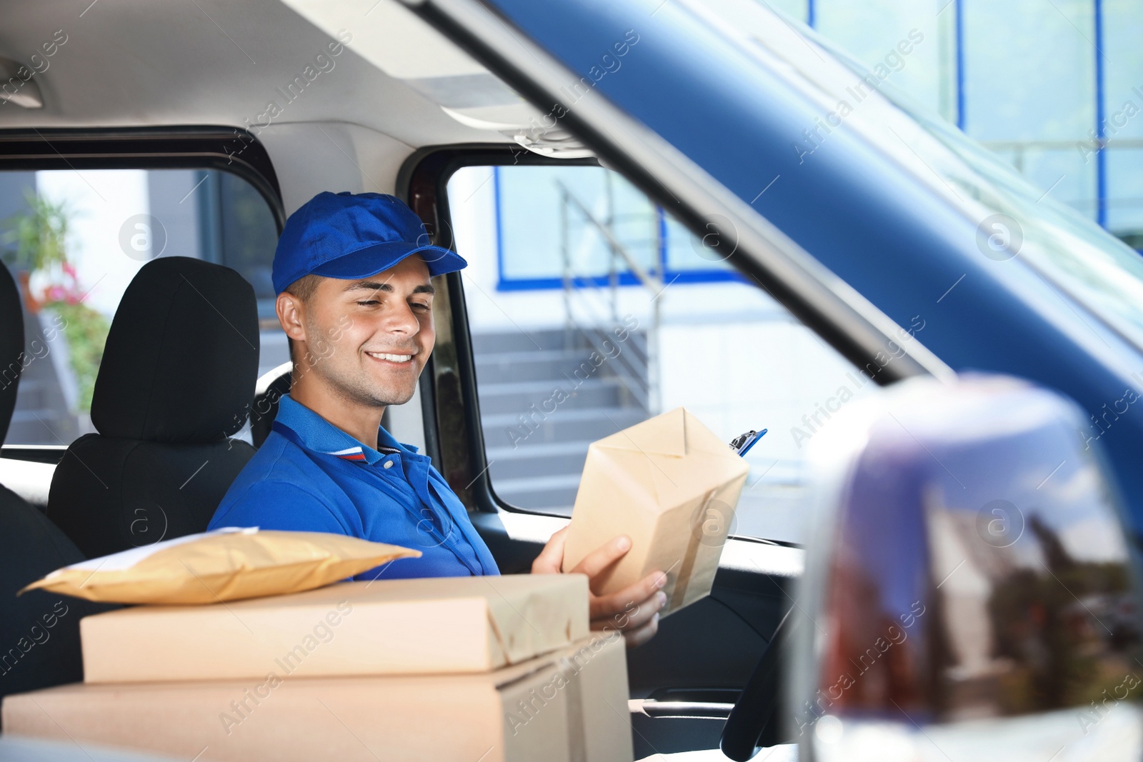 Photo of Young courier with parcels in delivery car