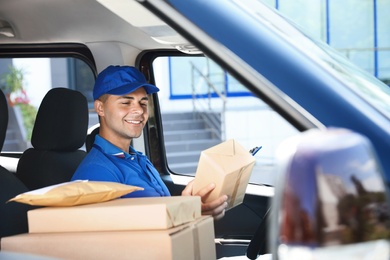 Young courier with parcels in delivery car