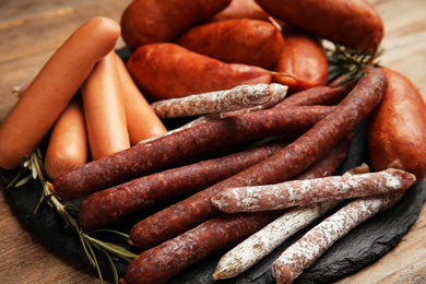 Different tasty sausages on wooden table, closeup