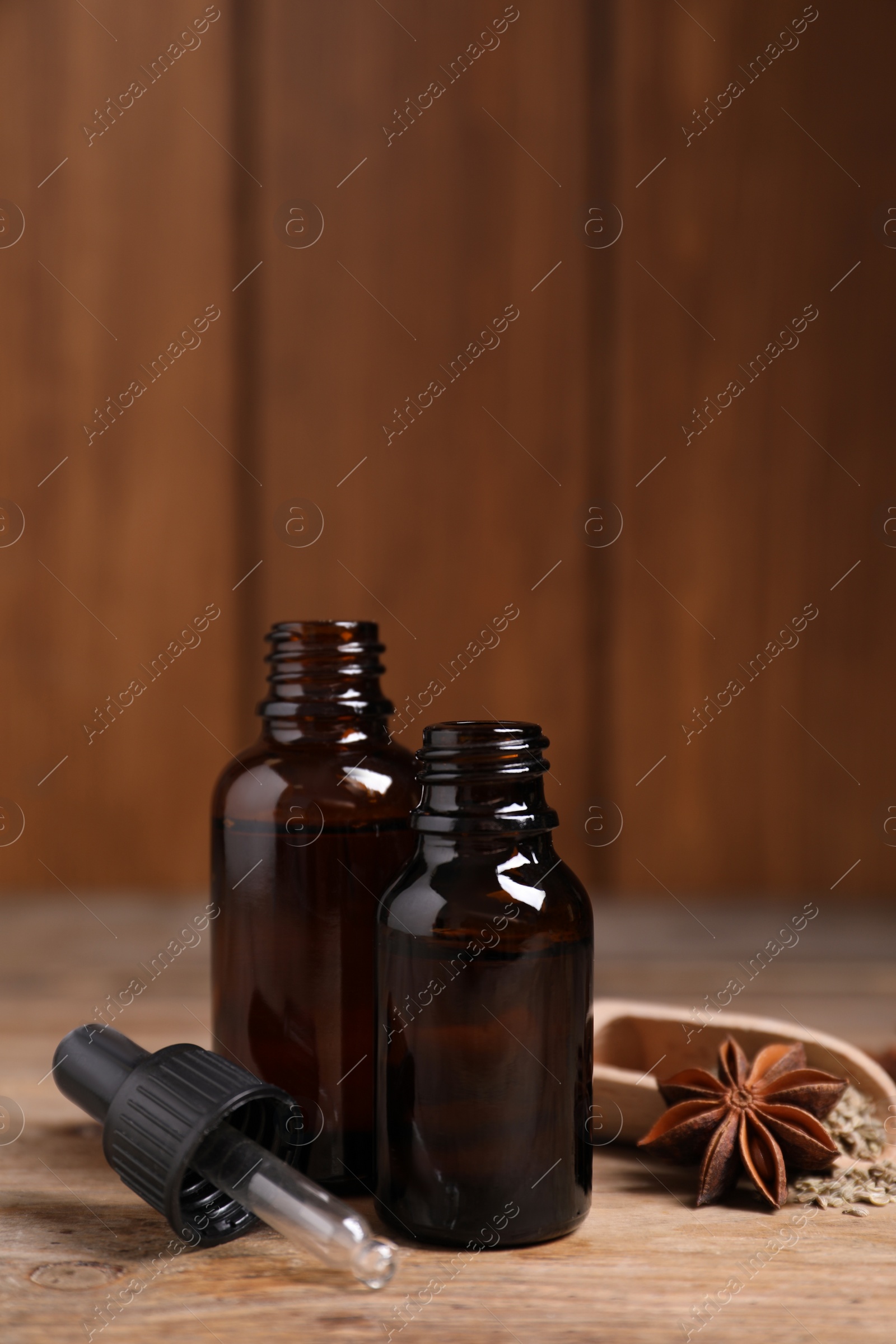 Photo of Bottles of essential oil, anise and seeds on wooden table