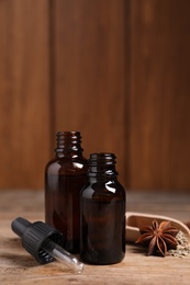 Bottles of essential oil, anise and seeds on wooden table