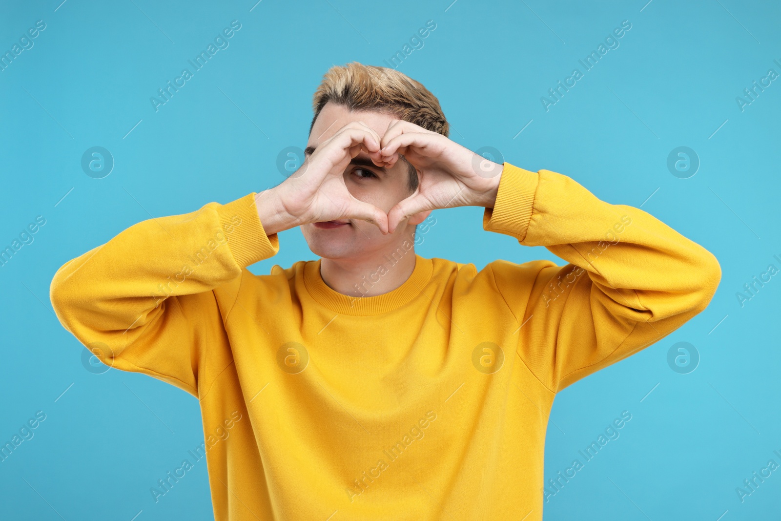 Photo of Young man showing heart gesture with hands on light blue background