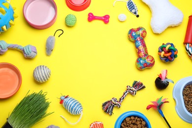 Different pet toys and feeding bowls on yellow background, flat lay. Space for text